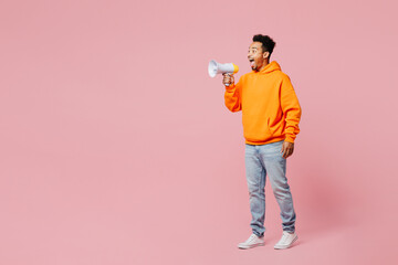 Full body young man of African American ethnicity wear yellow hoody casual clothes hold in hand megaphone scream announces discounts sale Hurry up isolated on plain pink background. Lifestyle concept.