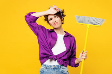 Young sad tired exhausted woman wears purple shirt casual clothes do housework tidy up hold broom...
