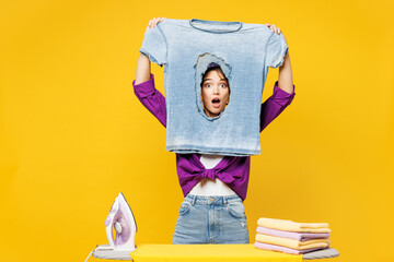 Young shocked sad mad woman wears purple shirt casual clothes do housework tidy up ironing look...