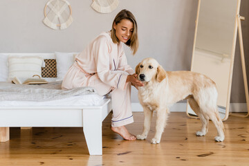 pretty smiling woman relaxing at home on bed in morning in pajamas with dog