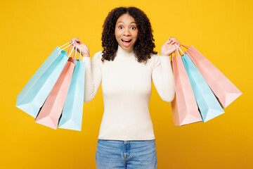 Little surprised shocked kid teen girl wears white casual clothes hold paper package bags after shopping look camera isolated on plain yellow background. Black Friday sale buy day lifestyle concept.