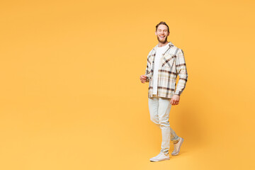 Fototapeta premium Full body side profile view smiling happy young Caucasian man he wear brown shirt casual clothes walking going look camera isolated on plain yellow orange background studio portrait Lifestyle concept