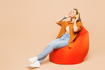 Full body young woman she wear orange shirt casual clothes sit in bag chair listen to tranquil...