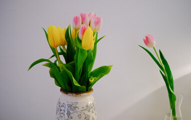 tulips in an old vintage vase against a white wall yellow and pink flowers in a vase on a table
