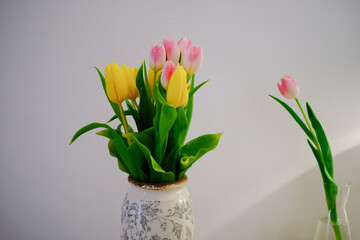 tulips in an old vintage vase against a white wall yellow and pink flowers in a vase on a table