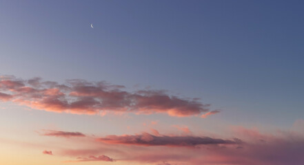 La Luna all’alba resta ancora nel cielo sopra le nuvole rosa 