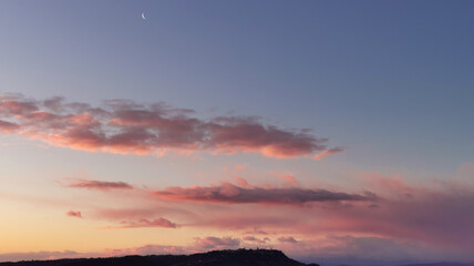 La Luna all’alba resta ancora nel cielo sopra le nuvole rosa sulla colline mentre il sole sorge...