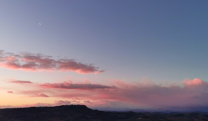 La Luna all’alba resta ancora nel cielo sopra le nuvole rosa sulla colline mentre il sole sorge...