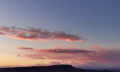 La Luna all’alba resta ancora nel cielo sopra le nuvole rosa sulla colline mentre il sole sorge dal mare
