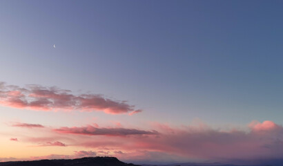 La Luna all’alba resta ancora nel cielo sopra le nuvole rosa sulla colline mentre il sole sorge...