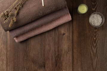 Fototapeta na wymiar Stack of towels with candle and sea salt on wooden background. Spa concept
