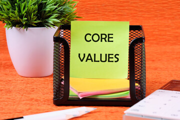 CORE VALUES word written on a green sticker next to office supplies on an orange background