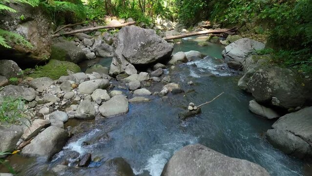 Drone photo. Panorama of a mountain river hidden in the rainforest jungle, bouncing water hitting the water surface, several huge rocks visible through splashes. Green leaves are moved by the wind