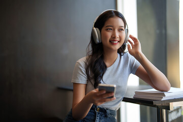 Asian teenage student woman wearing headphone to listening music and surfing social media on...