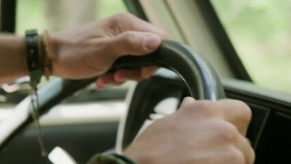 Close-up of hand of young unrecognizable man with wristbands holding by steer while sitting in car or camper van and driving to countryside for weekend trip