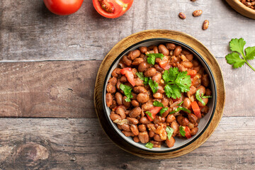 Food dish made of beans, tomatoes, and cilantro on a wooden table