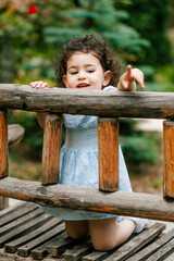 Child in blue dress kneeling and leaning on wooden railing and showing something