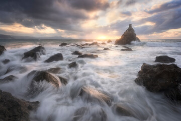 The sea water enters forcefully between the rocks of the shore on a warm sunset on the beach of Meñakoz, Sopelana, Bizkaia