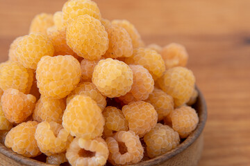 Yellow raspberries in a wooden bowl on the table. Summer berries background. Vitamin food, berry harvest. Healthy nutrition.