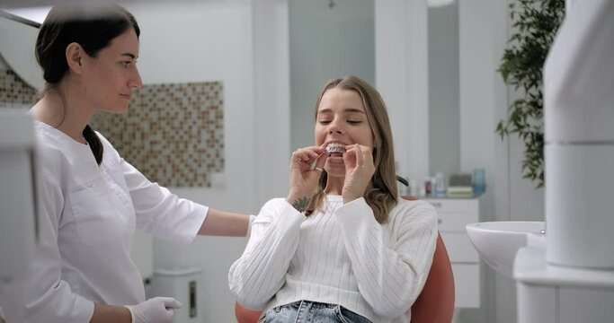 Charming Woman in a Dental Chair Measures Aligners, Dentist Shows Thumb with a Smile.