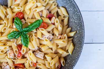 Italian pasta with swordfish, cherry tomatoes, oil and basil in a pan on a table Selective focue