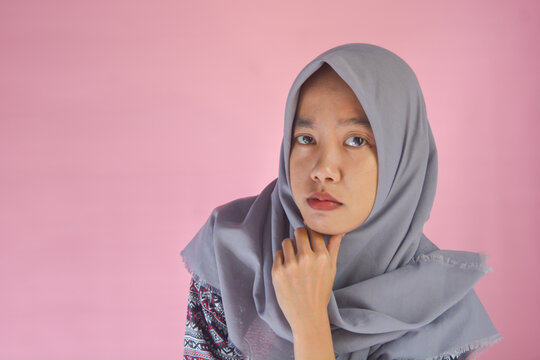 Photo of a young Indonesian woman with a creative style in a thinking position. Wearing batik clothes with a pink background