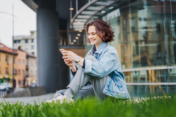 Young Caucasian woman using a smartphone while sitting near office building - 754866059