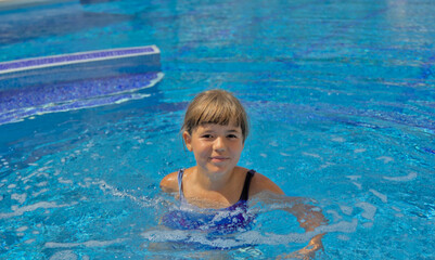 Fototapeta na wymiar A joyful child happily swimming and enjoying leisure time in an open pool with clear blue water. Active summer recreation in a resort with a swimming pool, embodying the essence of a happy childhood. 