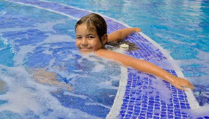 A joyful child happily swimming and enjoying leisure time in an open pool with clear blue water. Active summer recreation in a resort with a swimming pool, embodying the essence of a happy childhood.
