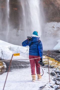 Female photographer from behind in winter in Iceland visiting the Seljalandsfoss waterfall
