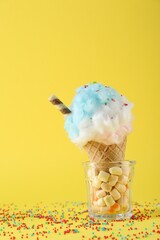 Sweet cotton candy in waffle cone on yellow background