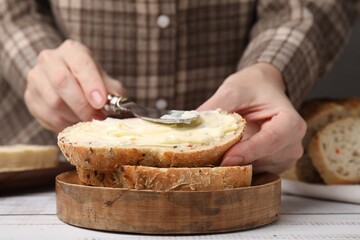 Woman spreading butter onto bread at white wooden table, closeup