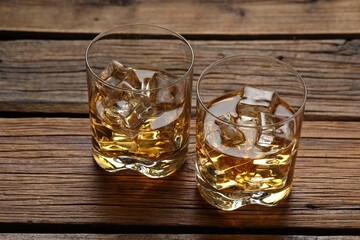 Whiskey with ice cubes in glasses on wooden table