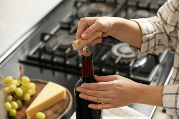 Woman opening wine bottle with corkscrew at countertop indoors, closeup