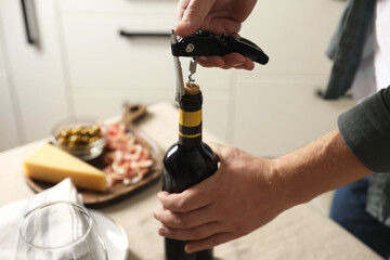 Man opening wine bottle with corkscrew at table indoors, closeup