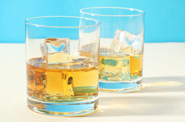 Whiskey with ice cubes in glasses on white table, closeup