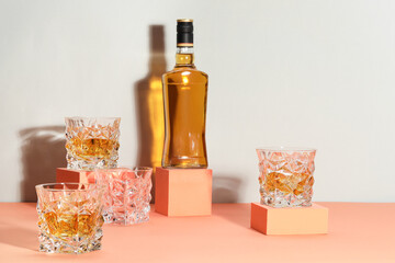 Stylish presentation of whiskey with ice cubes in glasses and bottle on color background