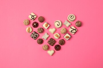 Heart made with delicious chocolate candies on pink background, top view