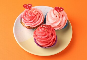 Delicious cupcakes with bright cream and heart toppers on orange background