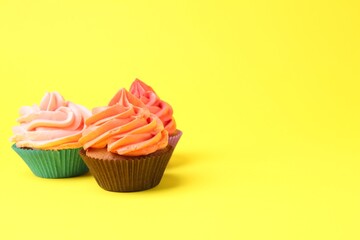 Delicious cupcakes with bright cream on yellow background. Space for text