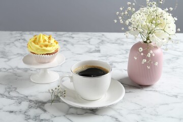 Delicious cupcake with yellow cream, coffee and flowers on white marble table