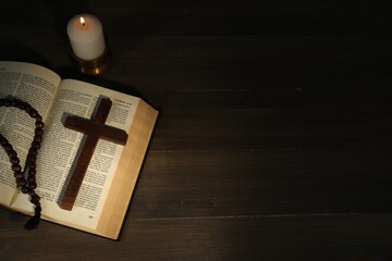 Church candle, Bible, rosary beads and cross on wooden table, top view. Space for text