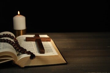 Church candle, Bible, rosary beads and cross on wooden table, closeup. Space for text