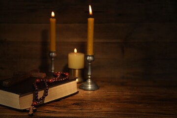 Church candles, cross, Bible and rosary beads on wooden table, space for text