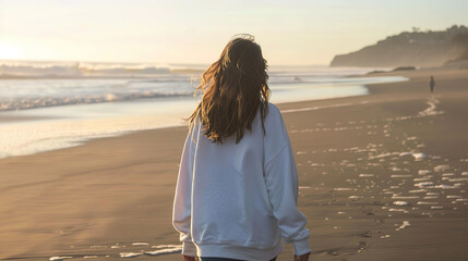 I want an image of a beautiful, natural looking girl walking down the beach in an oversized white crewneck sweatshirt, with empty copy space 