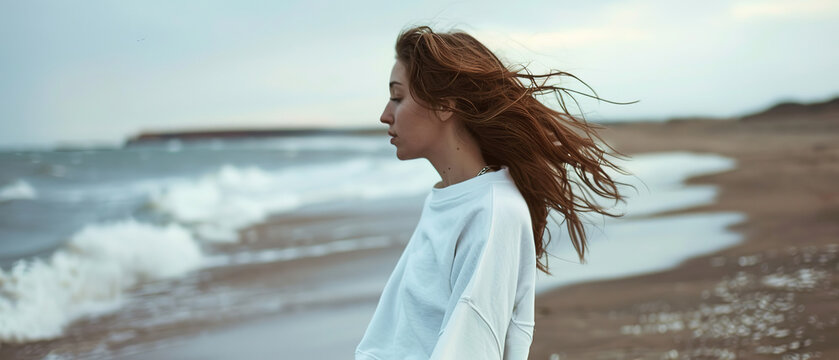 I want an image of a beautiful, natural looking girl walking down the beach in an oversized white crewneck sweatshirt, with empty copy space 