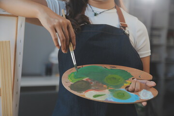 Cropped image of female artist standing in front of an easel and dipping brush into color palette