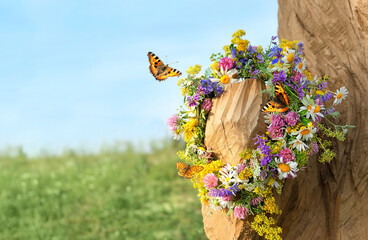 butterflies and colorful flowers wreath on tree on meadow. summer background. Floral crown, symbol of Summer Solstice Day, Midsummer holiday, Litha sabbat. witch, wiccan ritual. copy space - obrazy, fototapety, plakaty