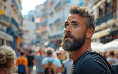 Obraz premium A man with a beard and blue eyes stands in a crowded street. He looks up at the sky, seemingly lost in thought. The scene is bustling with people, some carrying backpacks and handbags