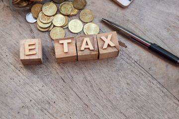 Business and e-tax concept. The word E TAX is written on the wooden cubes. A pile of coins, pen,...